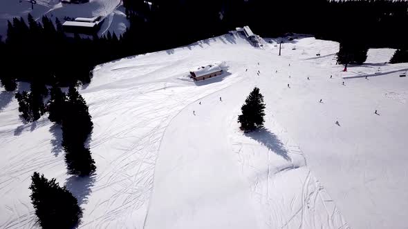 Aerial of ski resort at sun mountains with pine forest. Skiers ride down on snow slope at lifts. Win