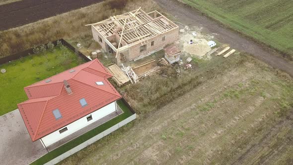 Top down aerial view of two private houses, one under construction with wooden roofing frame