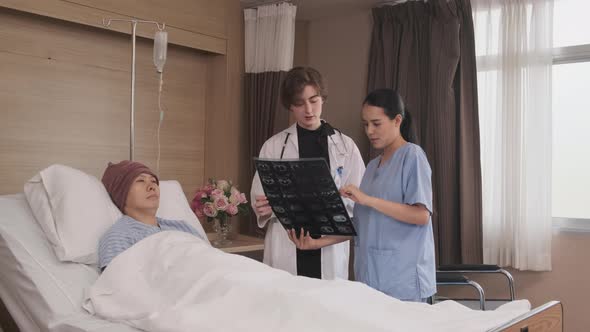 Female doctor explains x-ray film to patient at inpatient room bed in hospital.