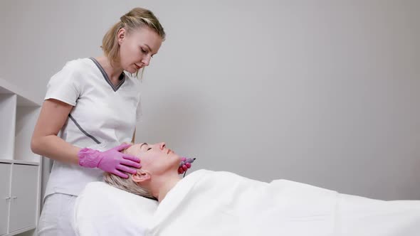 Professional beautician doctor in pink medical gloves making mesotherapy at client's face.