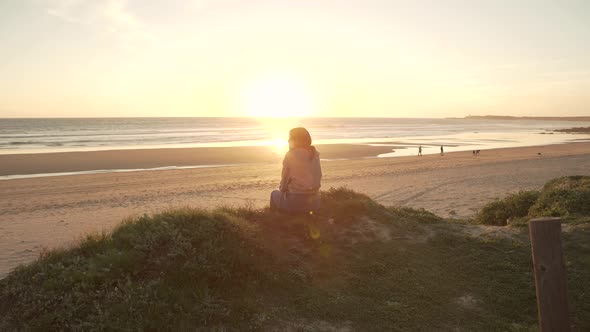 Traveling woman sitting on hill against sunset sky near sea