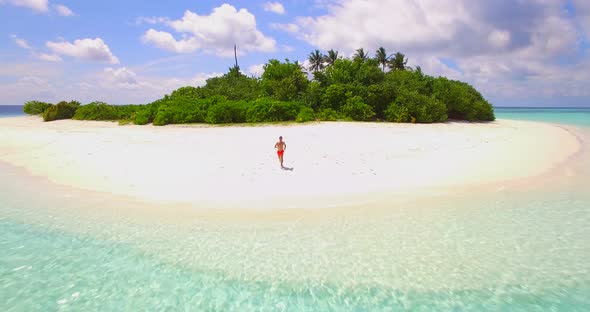 Aerial drone view of a man running, diving in and swimming on a small deserted tropical island