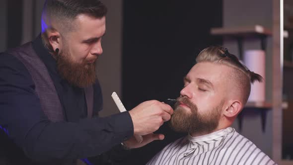 Stylish Hipster Client Man Visiting in Barber Shop. Shaving Beard By Professional Hairdresser.