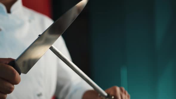 Restaurant kitchen: male chef sharpening knives before cooking steak