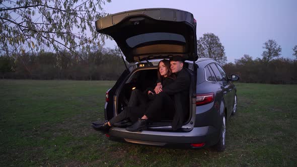 Full Body Young Couple Sitting Inside Open Trunk of Modern Vehicle