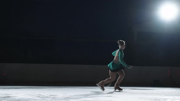 The Girl Skater Performs a Jump with the Rotation of a Triple Toe Loop in a Counter Light on an Ice