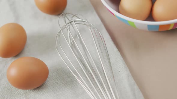 Video of overhead view of eggs and egg whisk on rustic cloth on beige background