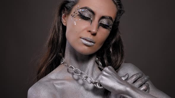 Woman with Silver Paint on Her Skin Face and Hair Poses in a Studio with Chain