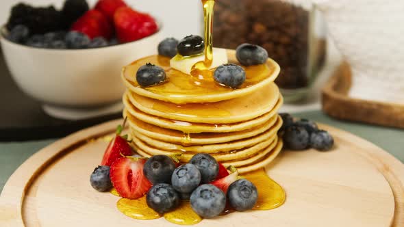 Pouring Honey or Maple Syrup on Pancakes with Berries on Top Closeup