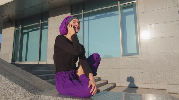 Islamic Muslim Woman Student Girl in Hijab Sitting on Background of City Building Outdoors Chatting
