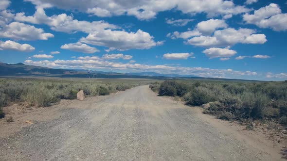 Small Asphalt Road Surrounded By Desert with Clouded Blue Sky.