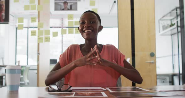 Smiling african american businesswoman at desk talking and gesturing during video call in office