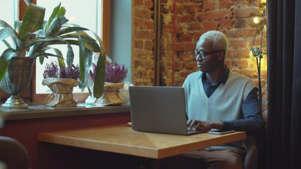 Black Man Drinking Coffee and Using Laptop in Cafe