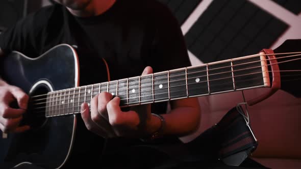 Young Man Playing Acoustic Guitar While Sitting on Sofa in Home Recording Studio