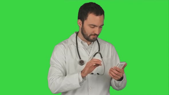 Medical Male Doctor Sending a Message with His Cellphone While Smiling and Standing on a Green