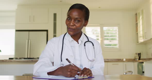 Smiling african american female doctor making notes during video call consultation