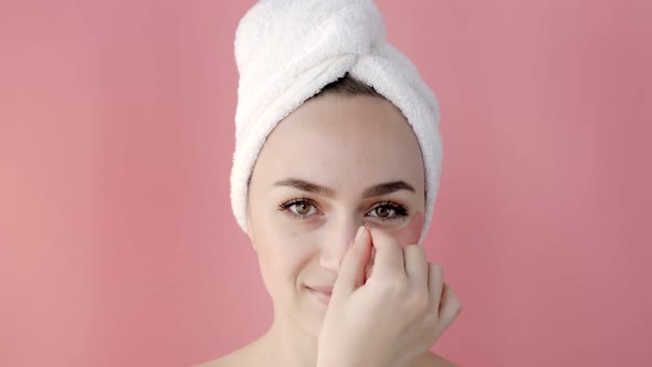 Plesant nude girl applying collagen eye masks on face in front of a mirror.