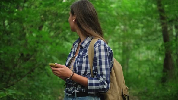 Young Female is Walking in Wood Holding Cellphone