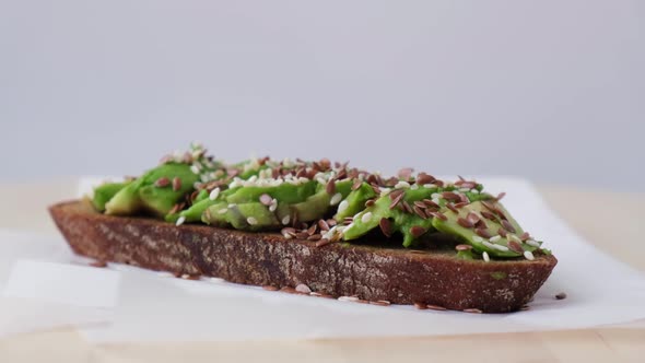 Healthy avocado toast rotating on wooden board. Sesame and flax seeds. Vegetarian food.