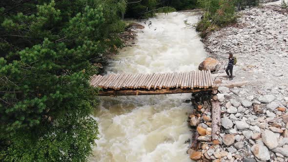 Woman Hiker Goes to River Wooden Bridge Between Rocky Banks