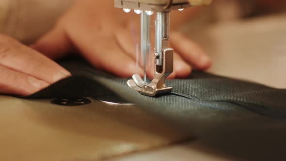 Hand of the seamstress is using white industrial sewing machine sew zipper