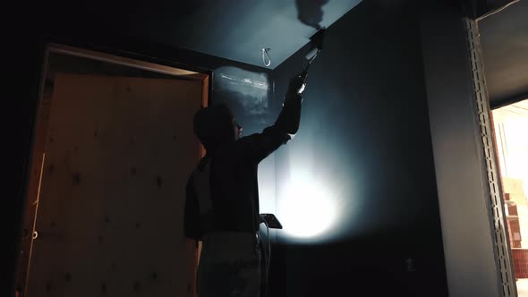 Painter on Construction Site Paints Walls in the Dark Illuminates with a Lamp