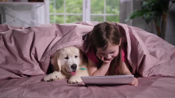 Little Girl Watching Cartoon with Puppy in Bed