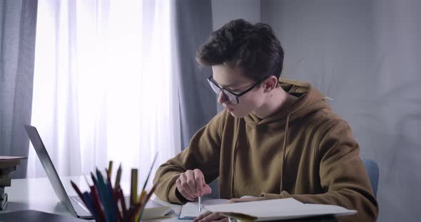Portrait of Clever College Student Comparing Information in Workbook and Online. Smart Nerd alt