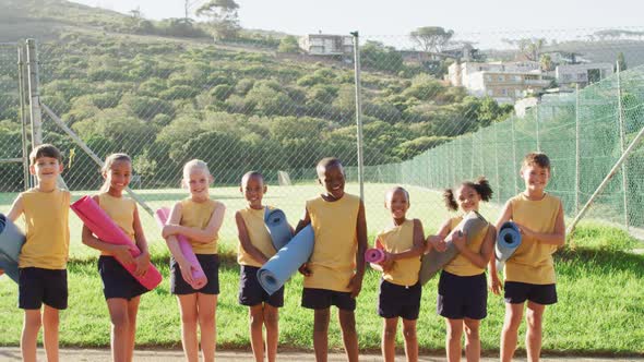 Diverse group of schoolchildren standing holding mats before yoga lesson outdoors