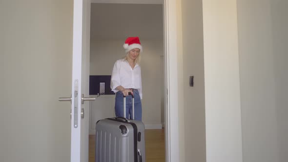woman in a Santa Claus hat enters the hotel with a suitcase and goes to window.