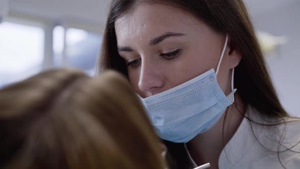 Dentist in Medical Mask Examining Teeth of Patient with Dental Tools in Clinic