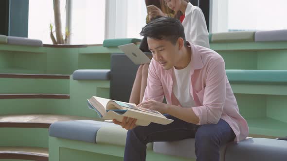 Young adult asian male university student in smart casual reading paper book preparing for test 