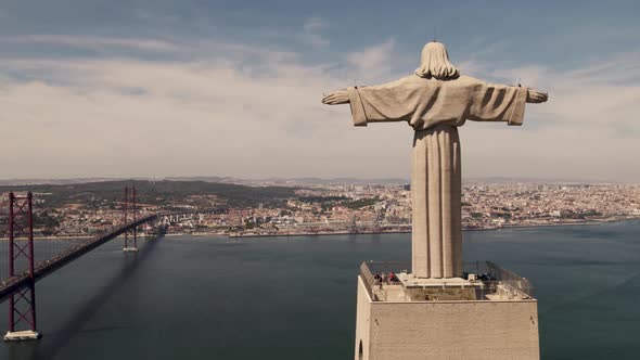 Establishing aerial shot of Christ the King overlooking Tagus river and Ponte 25 de Abril bridge.