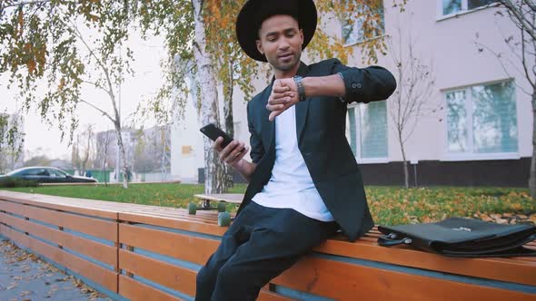 Young African Black Hipster Businessman with Longboard Using Smart Phone on Urban Background