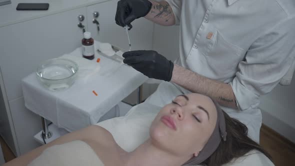 Male Tattooed Beautician Filling Syringe with Botox Filler As Blurred Beautiful Woman Lying on