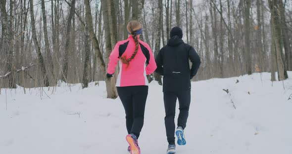 Positive Beautiful Young Healthy Couple Running with Sportswear Through the Forest in the Sunny