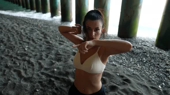 a Woman Dances at the Pillars of the Bridge on the Black Sand with the Incoming Waves