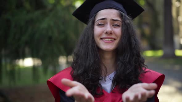 Front View Portrait of Excited Satisfied Smiling Woman in Graduation Toga and Mortarboard Cap