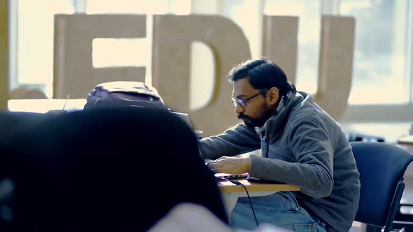 Young American Man is Working with Laptop at Table in Modern Office Irrl