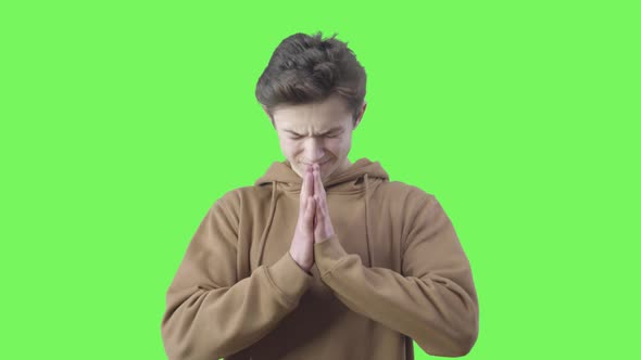 Desperate Boy Praying at Green Background. Portrait of Teenage Brunette Caucasian Believer with alt