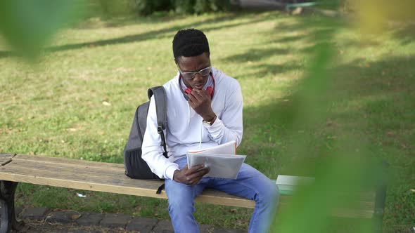 Busy Concentrated African American Student Learning Outdoors Sitting on Bench at College Yard