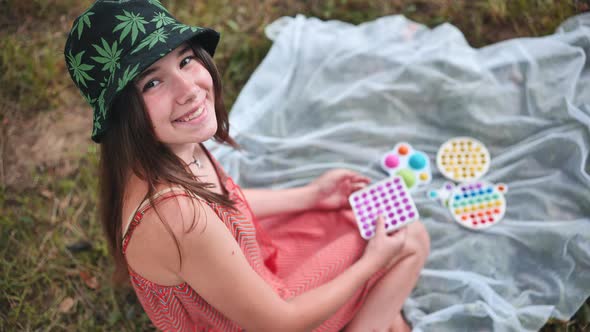 Smiling Girl Plays with Antistress Toys Popit and Simple Dimple in the Park on a Summer Day