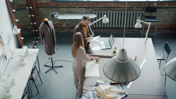 Top View of Girl and Guy Tailors Working Together Talking and Measuring Material in Studio