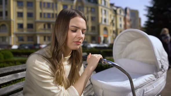 Exhausted Mother Falling Asleep While Swinging Newborn Carriage Sitting on Bench