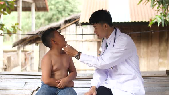 Male Doctor Examining Poor Child Mouth At Countryside