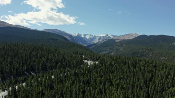 Aerial view moving from forest highway to alpine lake to mountain range, 4K