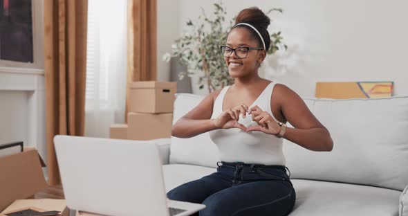 Young Woman Sits on Sofa in Apartment and Talks to Friend Through Laptop Webcam They Gossip Laugh