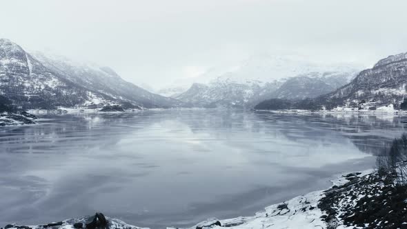 Flying above a frosen lake between Mountains in fogy day in Norway in december 2018