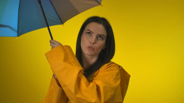 A Happy Charming Woman in a Yellow Raincoat is Rotating a Rainbow Umbrella