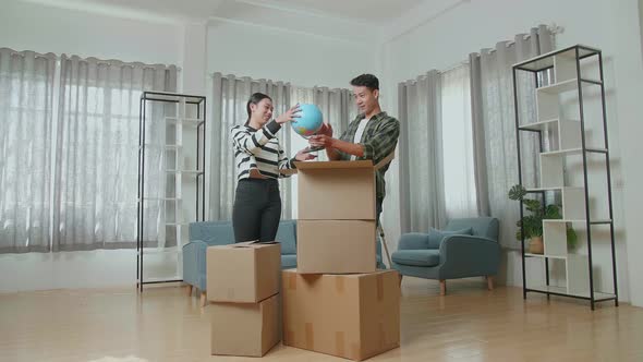 Asian Couple Moving Into A New House Unpacking The Cardboard Boxes And Taking Stuff Out Of Them